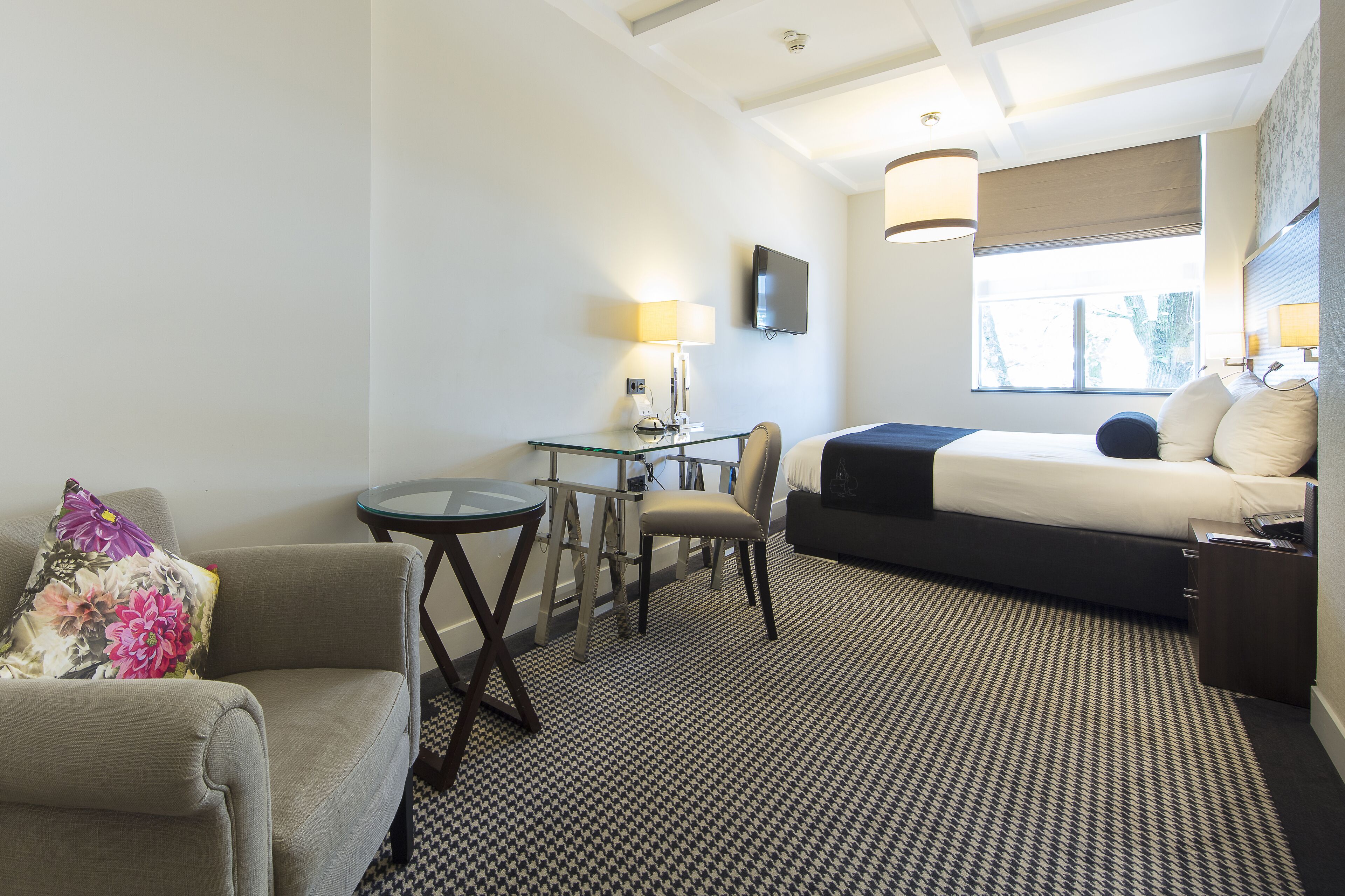 A hotel room with a bed, a desk, a chair, a sofa, and a TV.
