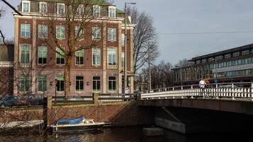 A canal with a bridge, a boat, and a building with multiple windows and a green roof.