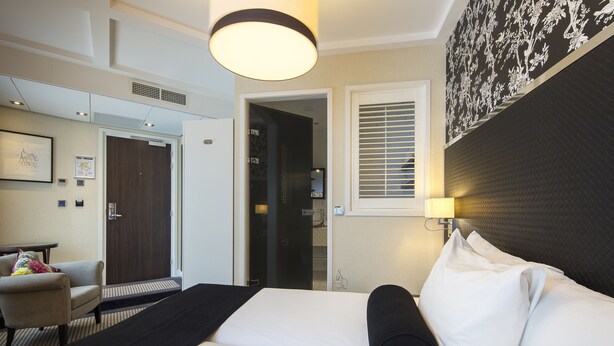 Una habitación de hotel con una cama, una silla, un escritorio y una puerta que da a un baño.