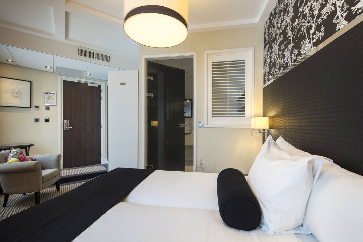 A hotel room with a bed, a chair, a desk, and a door leading to a bathroom.