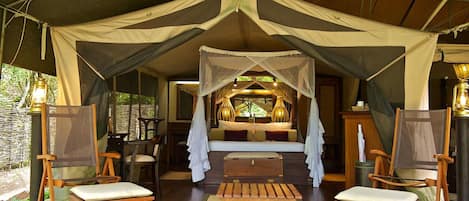 A tented accommodation with a bed, two wooden chairs, a small table, and a bench.