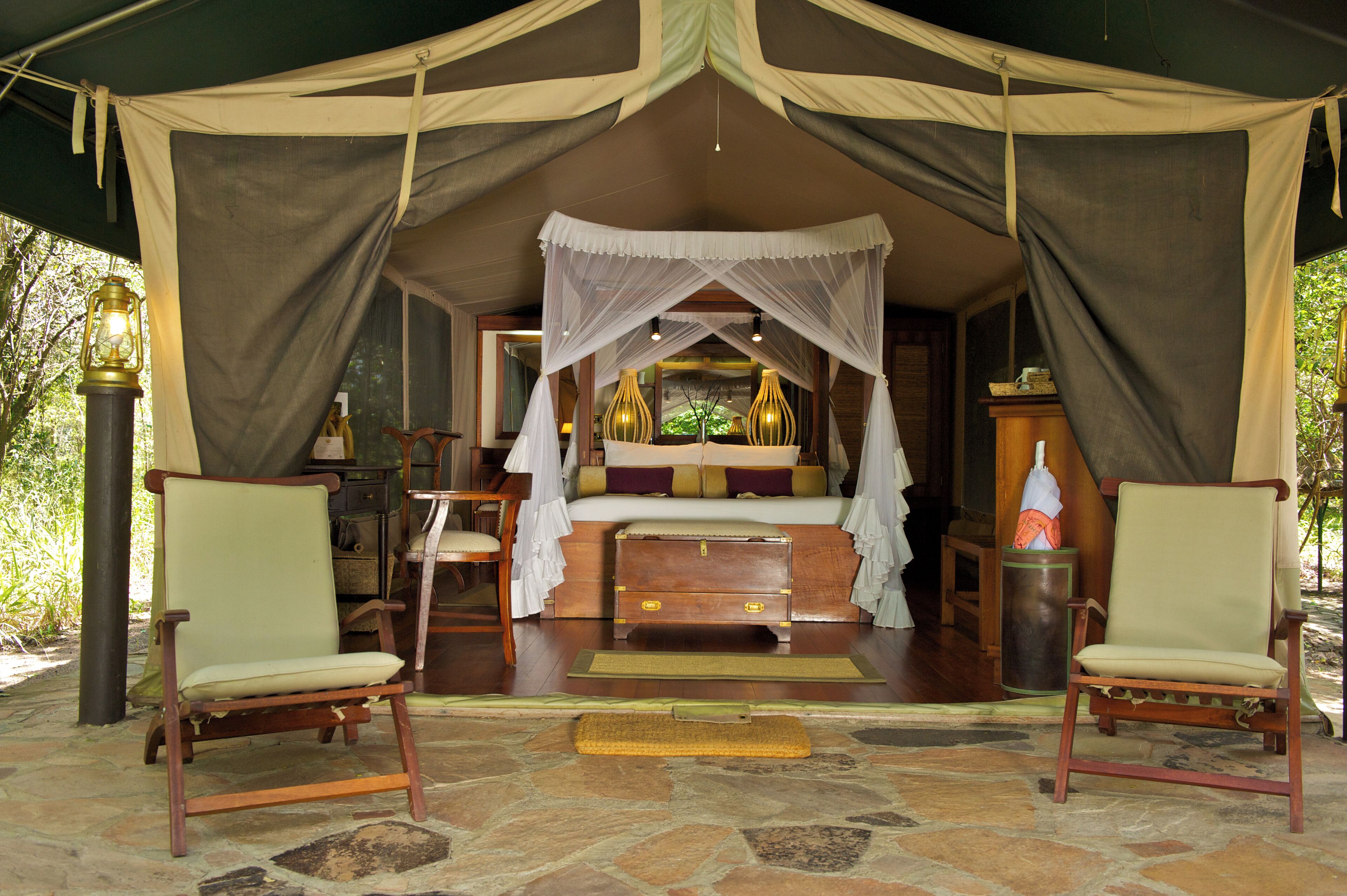 Quarto com tenda, uma cama, duas cadeiras, uma mesinha de cabeceira e um abajur.