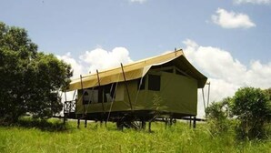 A single-story tent-style building with a pitched roof, surrounded by tall grass and trees. - Mara Intrepids Tented Camp (Maasai Mara)