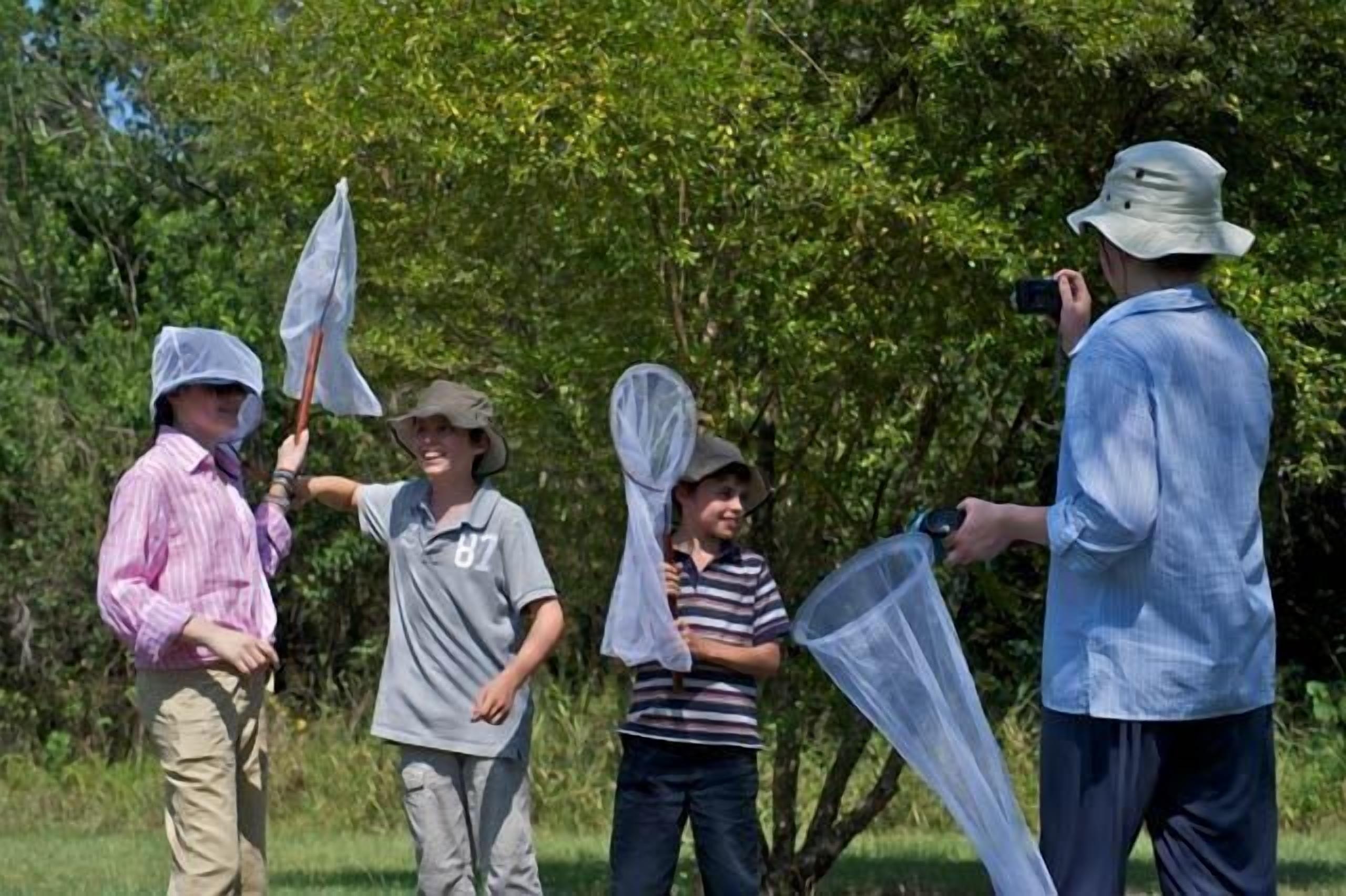 A group of people outdoors, some holding nets, possibly engaged in an activity like bird watching or fishing.