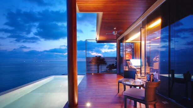A modern outdoor deck with a view of the sea, a glass wall, and a seating area. - Impiana Private Villas Kata Noi (Karon)