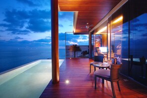 Una terraza moderna al aire libre con vista al mar, un muro de cristal y una zona de estar.