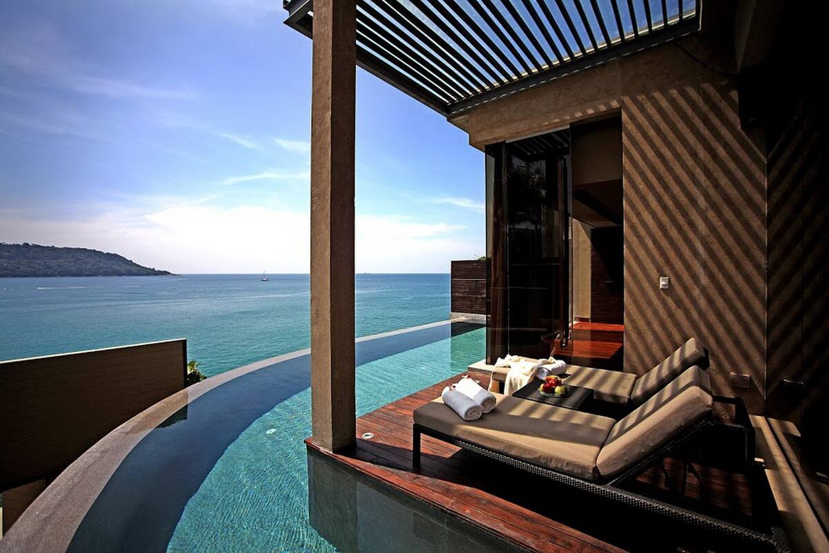A infinity pool with a view of the ocean, a lounge area with a sofa and table, and a modern architectural design.