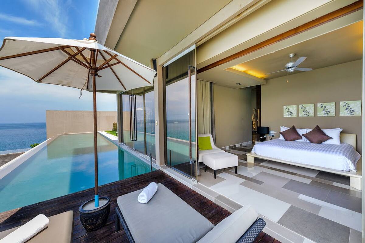 A modern hotel room with a balcony, a bed, a seating area, and a view of the sea.