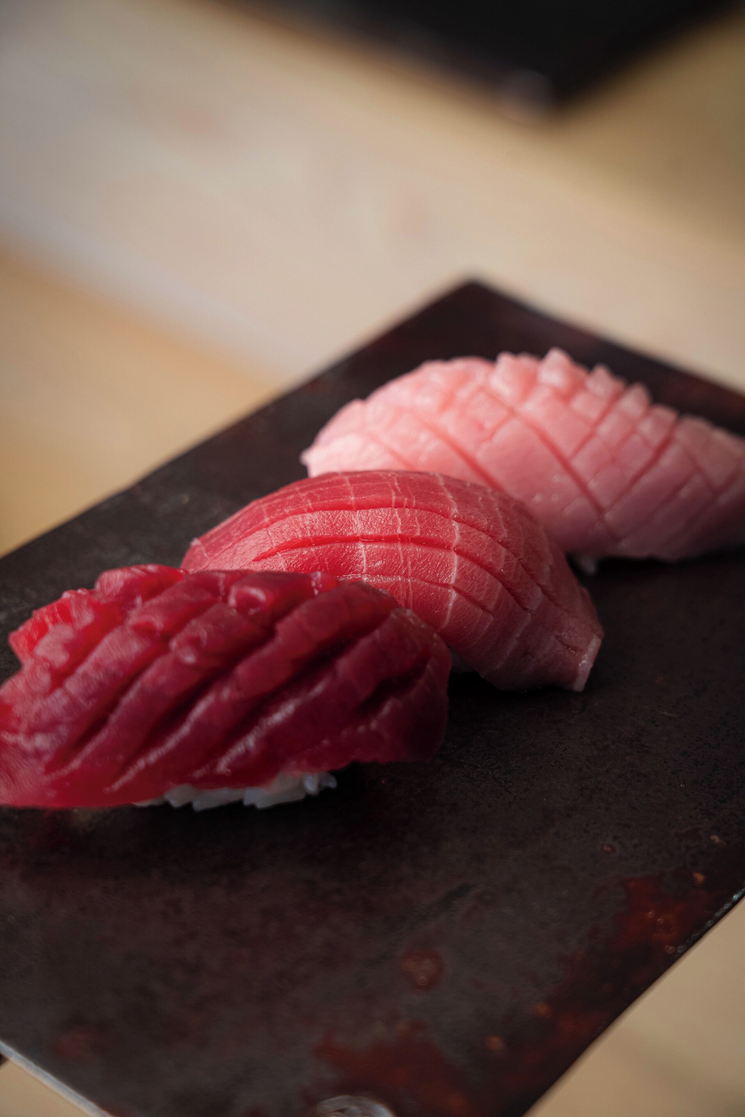 A close-up of three pieces of sushi on a dark plate.