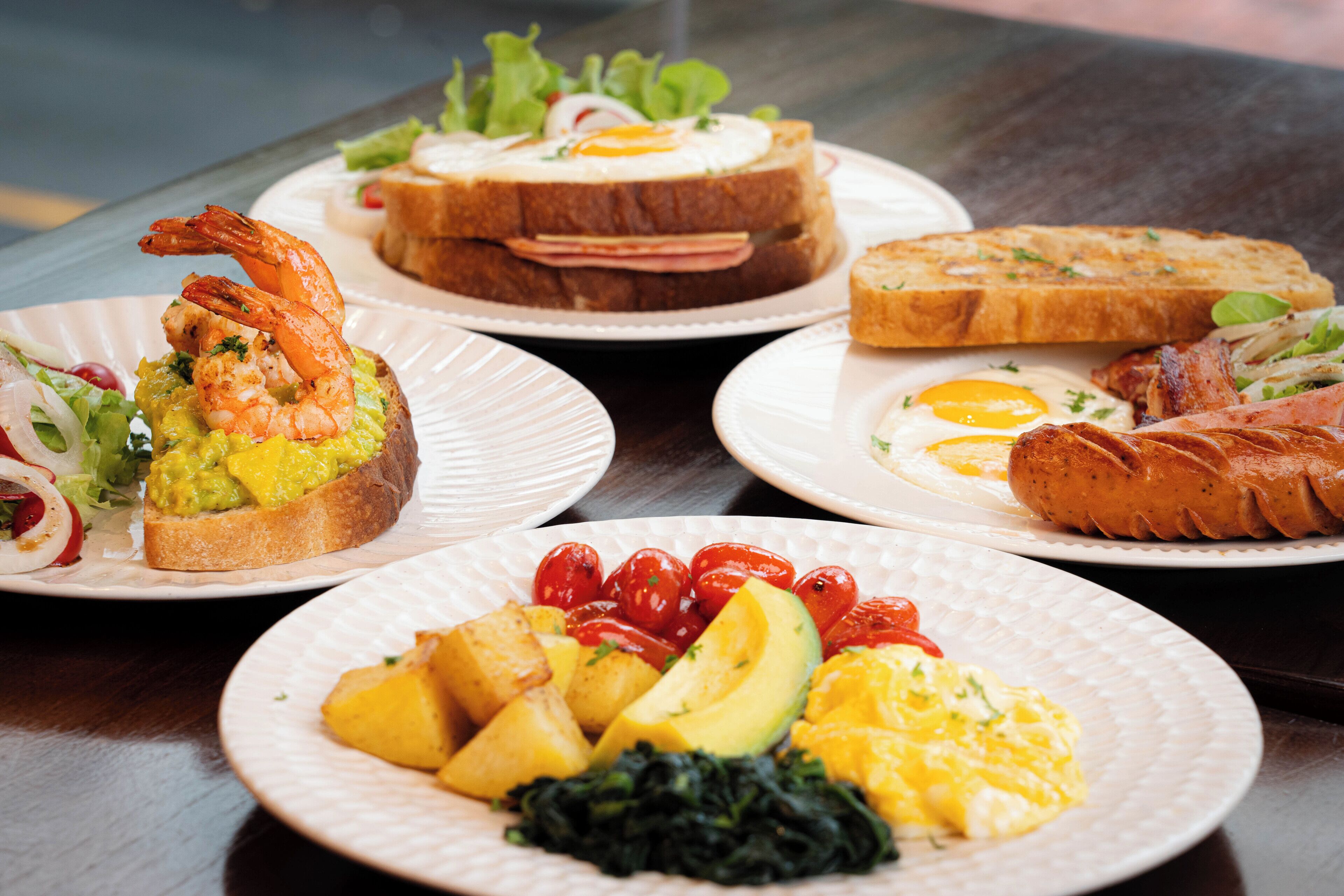 A table with various breakfast dishes including toast, eggs, shrimp, and vegetables.