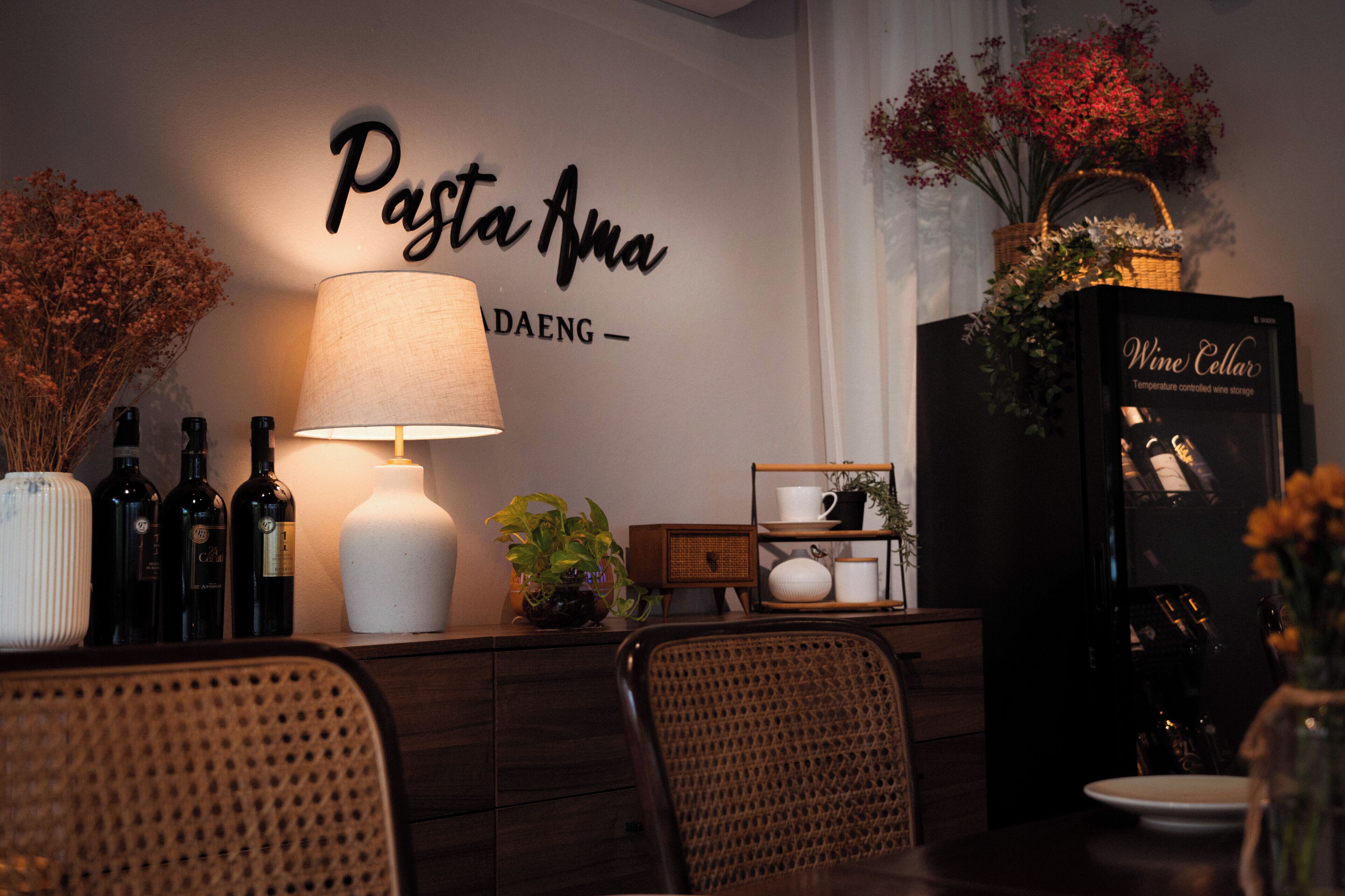 Un comedor con un letrero en la pared que dice "Pasta Anna", una mesa con sillas, una lámpara y un enfriador de vino.