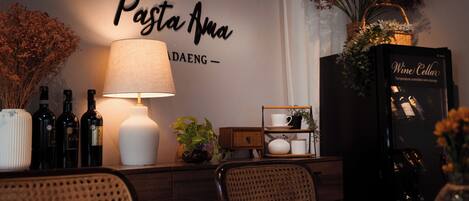 Un comedor con un letrero en la pared que dice "Pasta Anna", una mesa con sillas, una lámpara y un enfriador de vino.