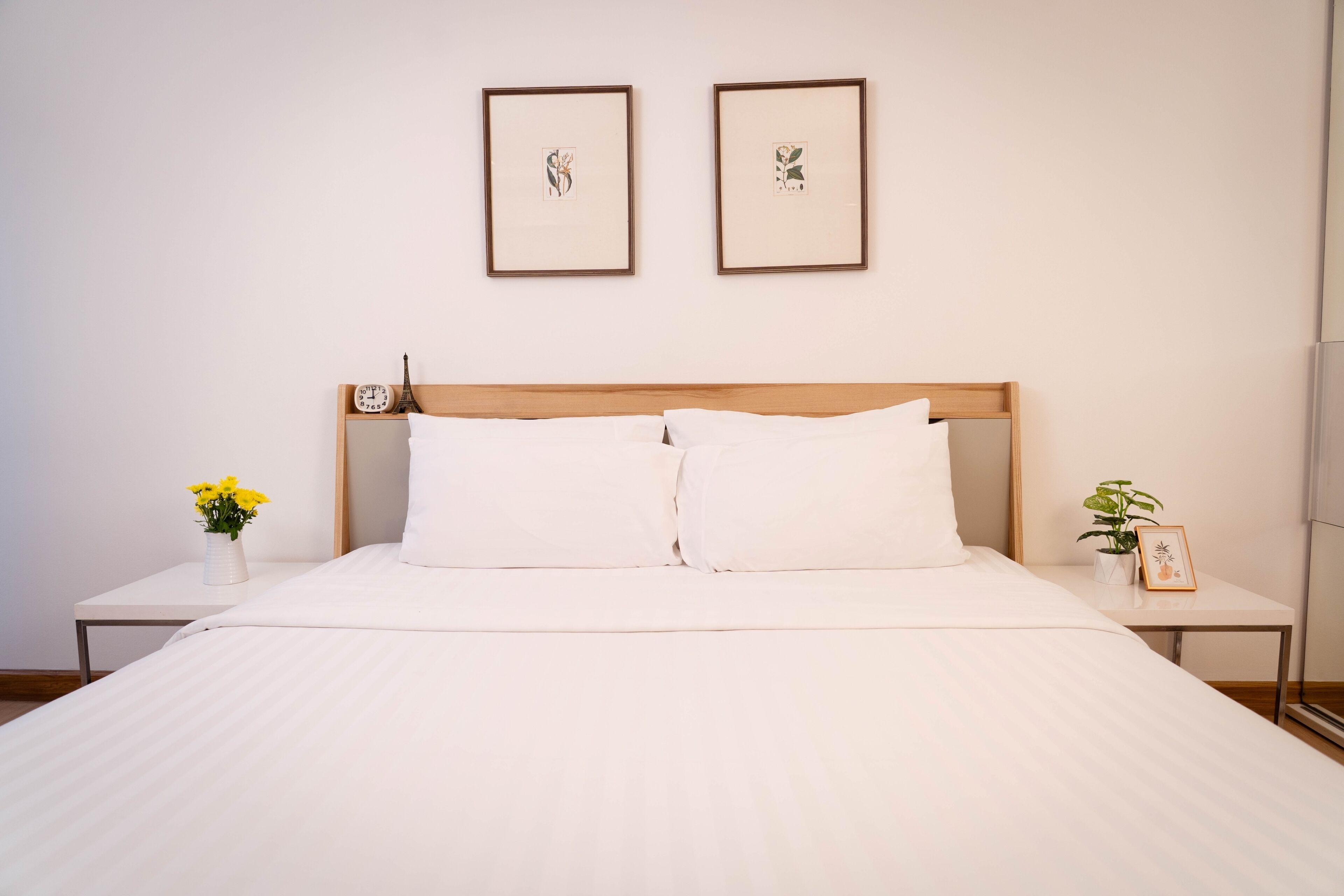 A neatly made bed with white linens, a wooden headboard, and two framed pictures on the wall.