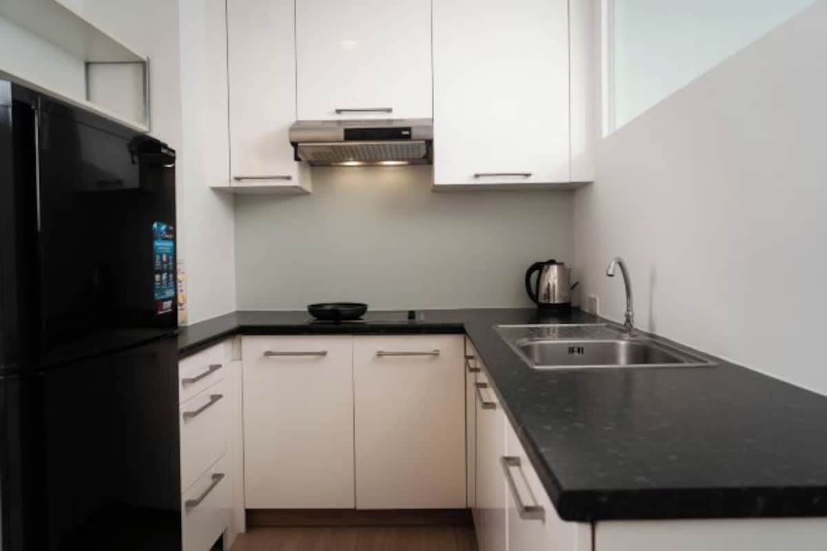 A modern kitchen with white cabinets, a black countertop, a stainless steel sink, and a black refrigerator.
