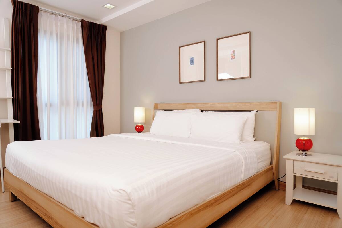 A neatly made bed with white linens, two bedside lamps, and a nightstand with a red lamp.
