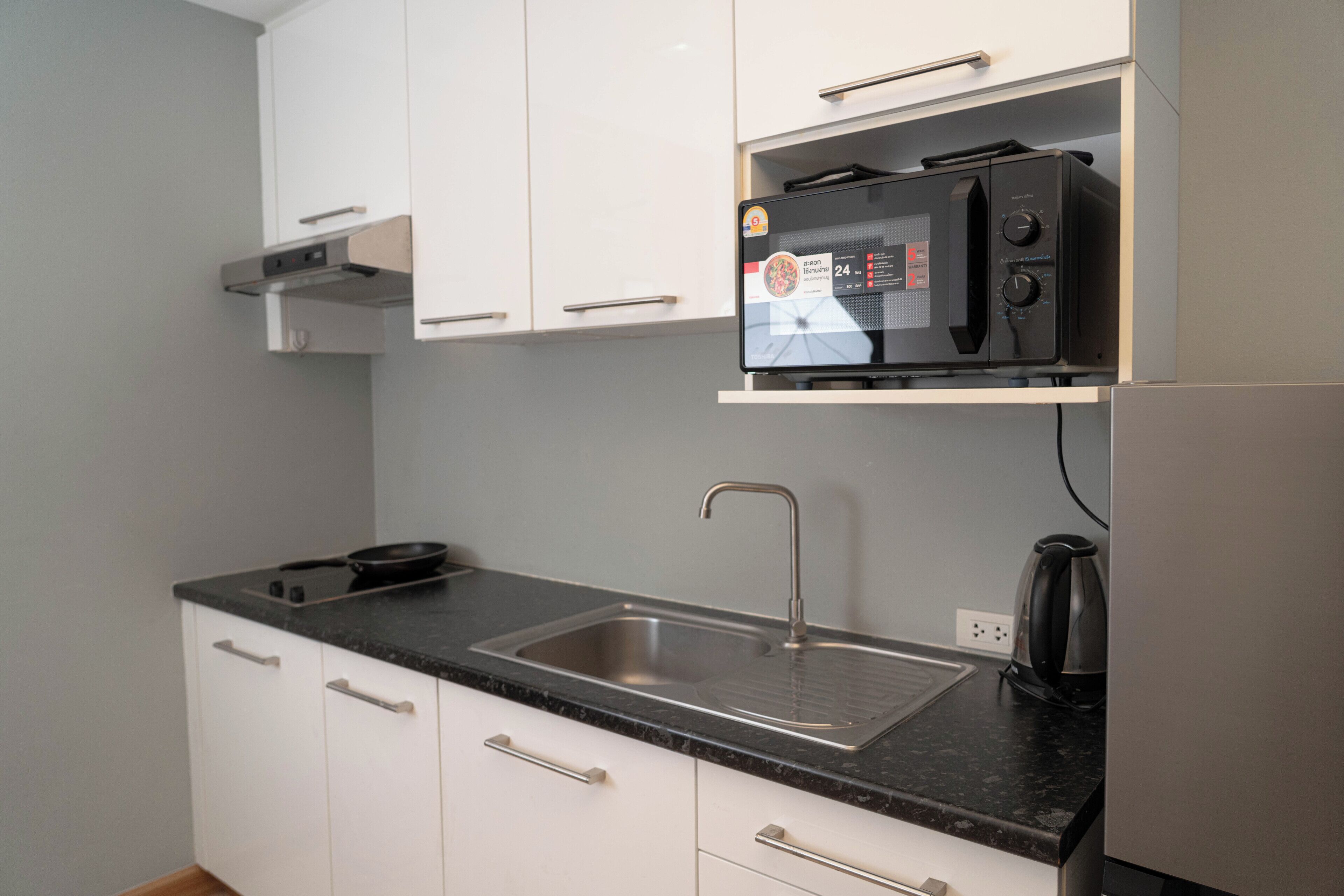 A kitchen with white cabinets, a stainless steel sink, and a microwave on a countertop.