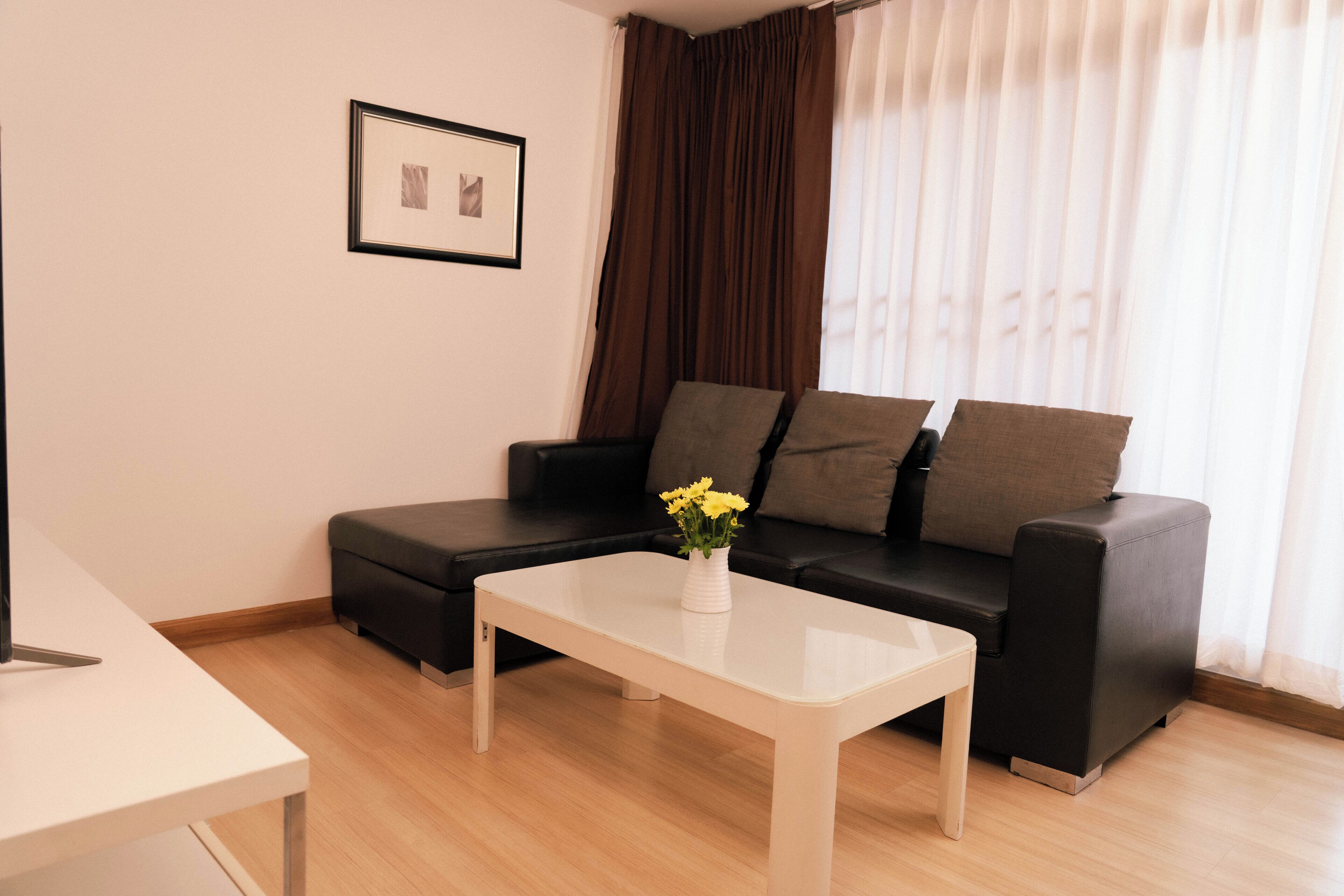 A modern living room with a white coffee table, a black sofa with cushions, a framed picture on the wall, and a window with curtains.