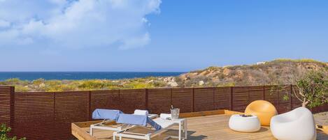 Terraza de madera con sillones de descanso y un espacio de estar moderno con vistas al paisaje costero.