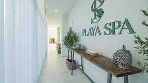 A hallway with a reception desk, a wall sign reading "PLAYA SPA", and potted plants.
