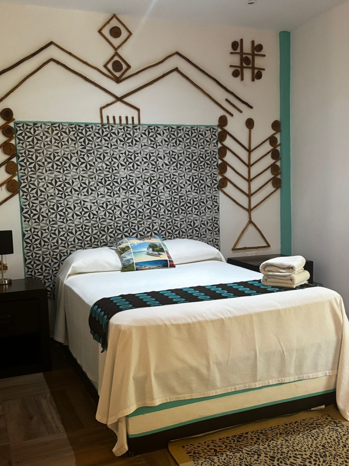 Una cama bien hecha con un cabecero estampado, una almohada con un motivo panorámico y una toalla doblada al lado.