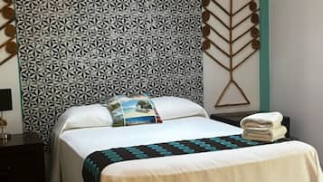 Una cama bien hecha con un cabecero estampado, una almohada con un motivo panorámico y una toalla doblada al lado.