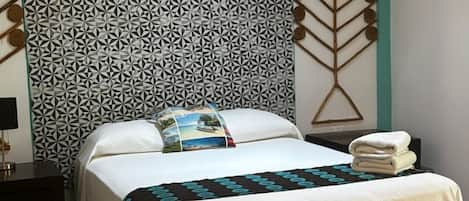 Una cama bien hecha con un cabecero estampado, una almohada con un motivo panorámico y una toalla doblada al lado.