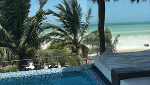 A pool area with a view of the beach, palm trees, and a thatched roof structure. - Villas Tiburon Adults only (Isla Holbox)