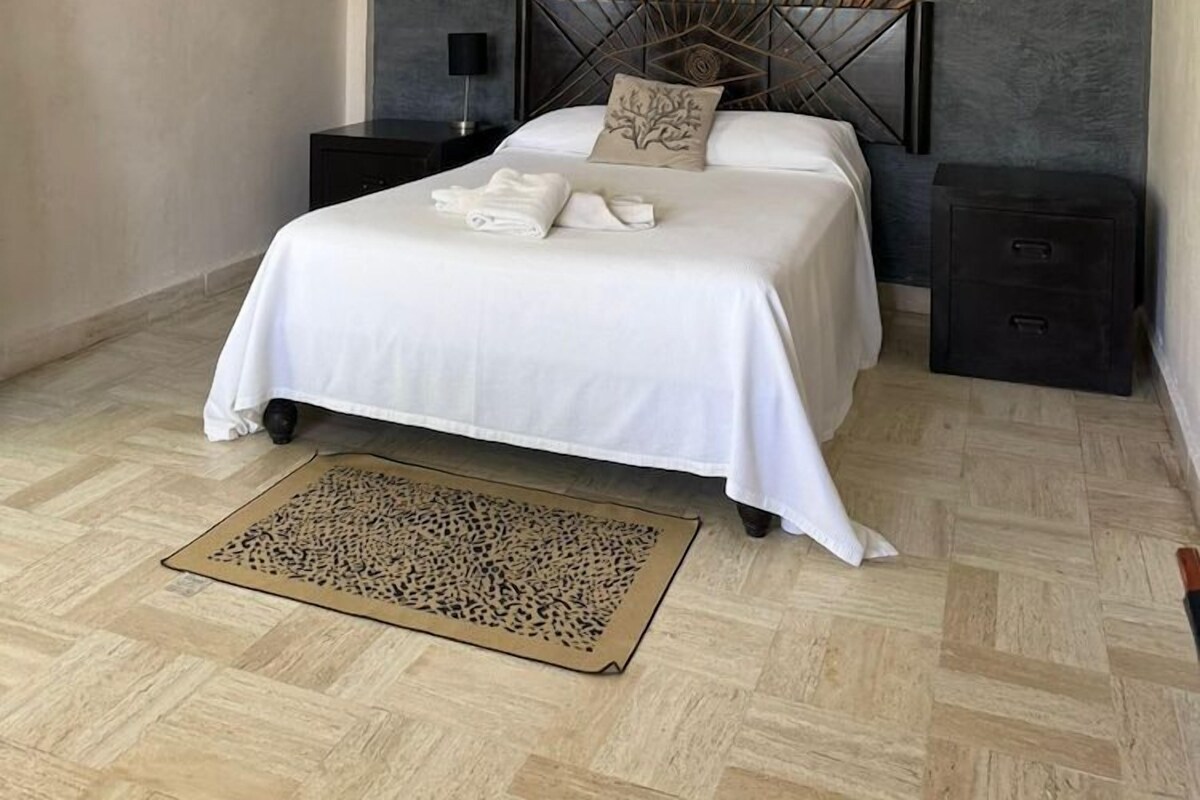 Een moderne slaapkamer met een bed, nachtkastjes, een decoratief wandpaneel en een kamerkleed met dessin.