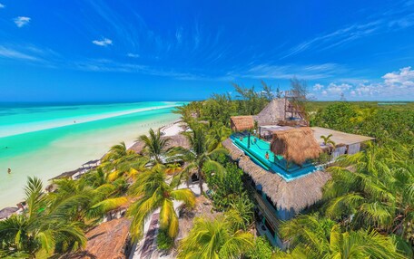 A tropical resort with a pool, thatched-roof structures, and a beach view.