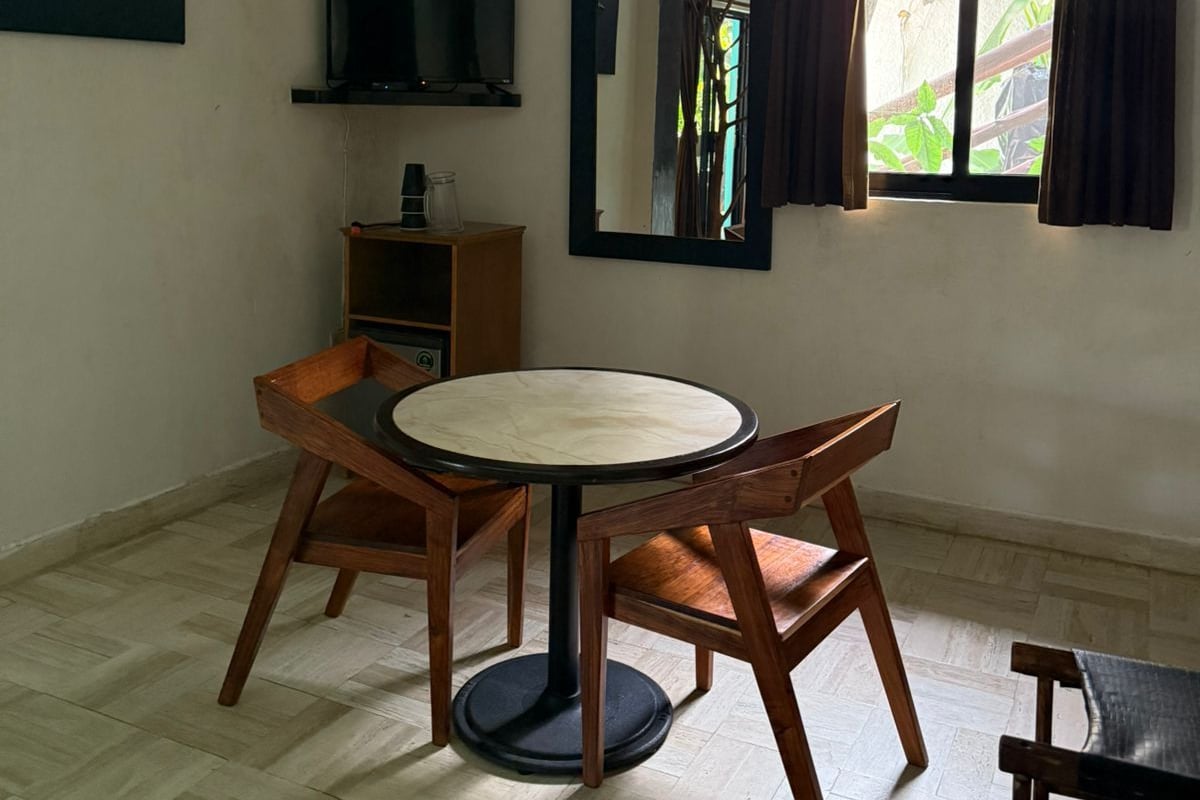 Een kamer met een ronde tafel, twee houten stoelen, een televisie, een boekenkast, een spiegel en een raam met gordijnen.
