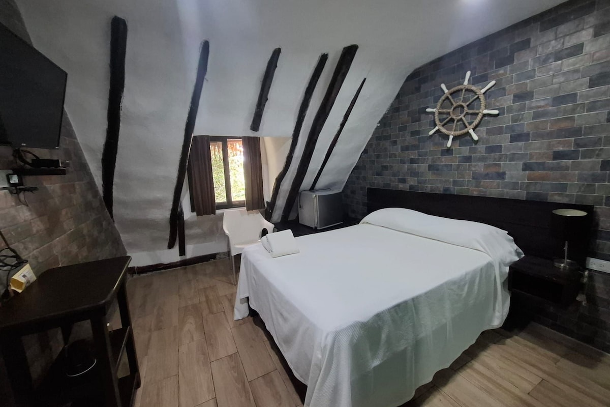 Een slaapkamer met een schuine kap, een bed, een bureau, een stoel en een aan de muur bevestigd scheepsroer.