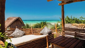A wooden deck with a thatched-roof hut, a bench, and a bed with zebra-patterned pillows. - Villas Tiburon Adults only (Isla Holbox)