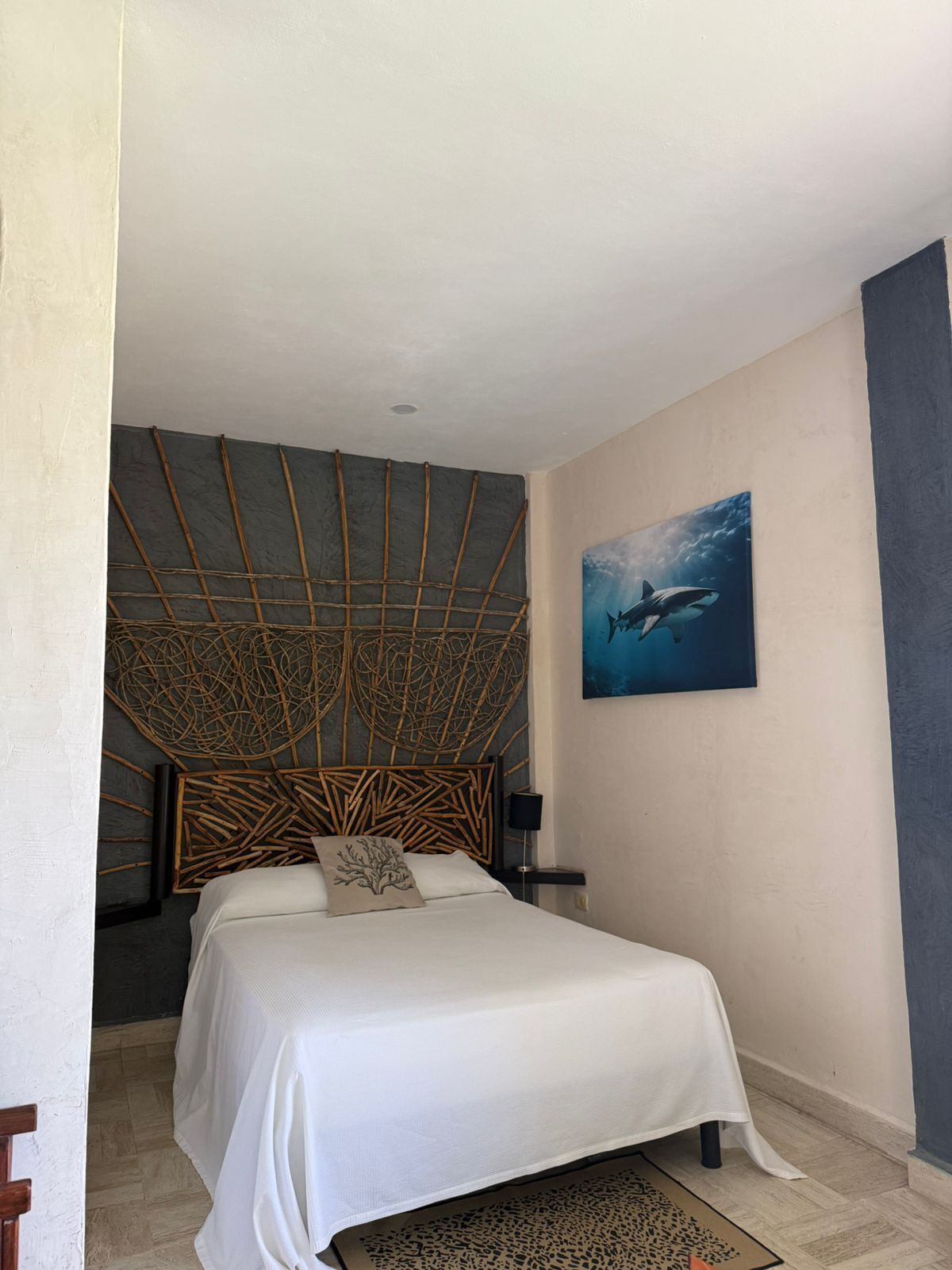 A bedroom with a bed, a wall-mounted artwork of a shark, and a unique woven headboard.