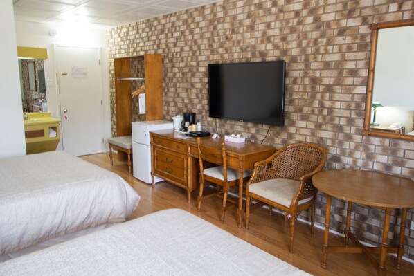 Une chambre d’hôtel avec deux lits, un bureau en bois, une chaise, une télévision et un mur décoré d’un motif en briques.
