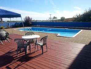 A swimming pool with a wooden deck, surrounded by chairs and a table. - Auberge La Rocaille (Shawinigan)