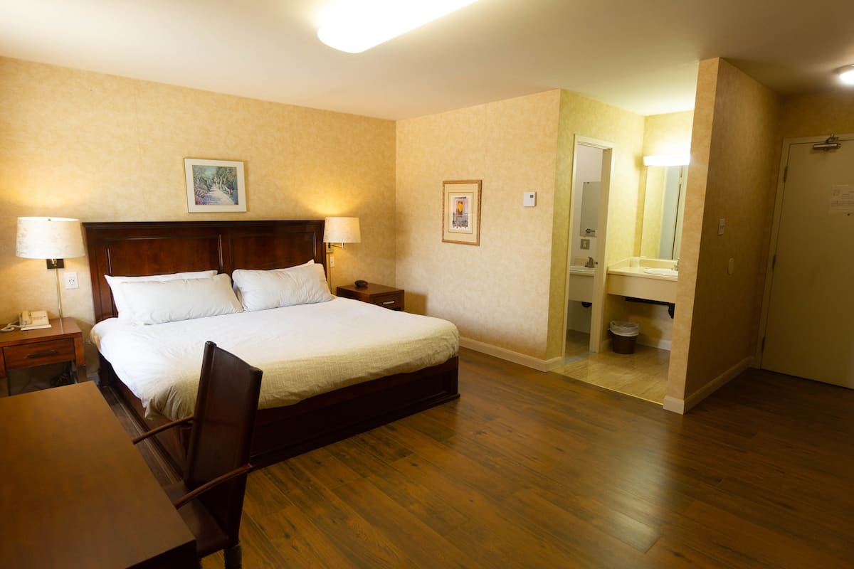 Habitación de hotel con cama de madera, lámparas de noche, escritorio y baño con espejo y lavamanos.