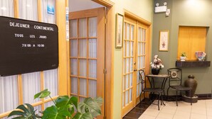A hotel lobby with a reception desk, a wooden door, a small table with chairs, and a potted plant. - Auberge La Rocaille (Shawinigan)