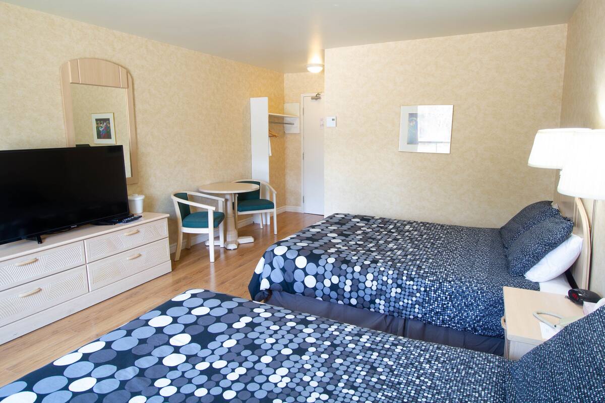 Habitación de hotel con dos camas, un escritorio, una silla, un televisor y una lámpara.