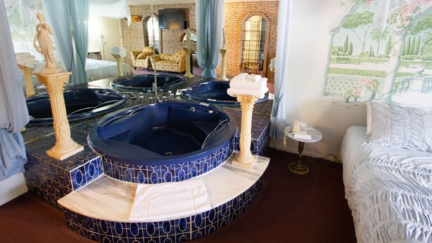 A bathroom with four large tubs, a mirror, a bed, and a wall with a floral mural. - Auberge La Rocaille (Shawinigan)