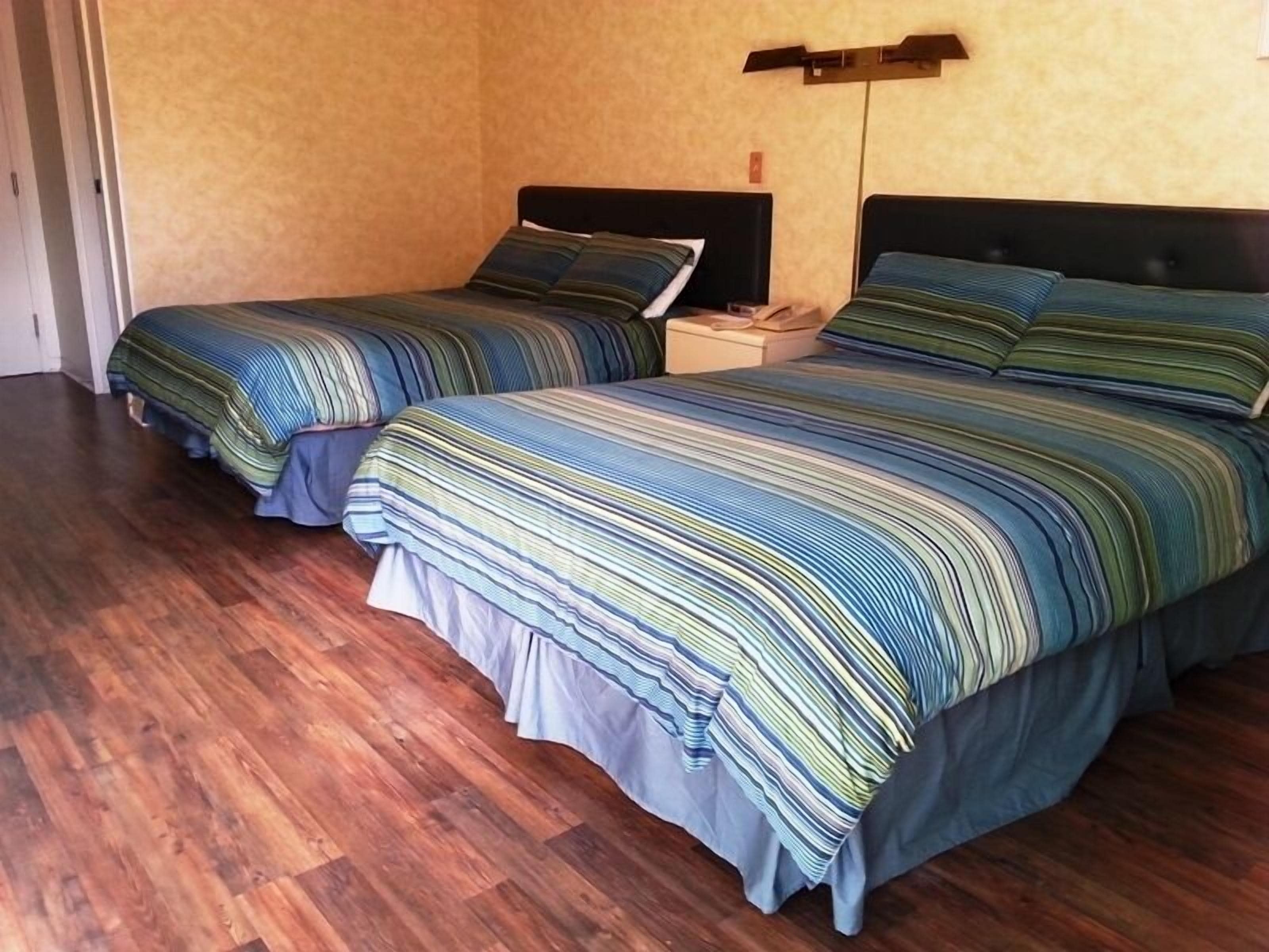 A room with two beds, wooden flooring, and a light-colored wall.