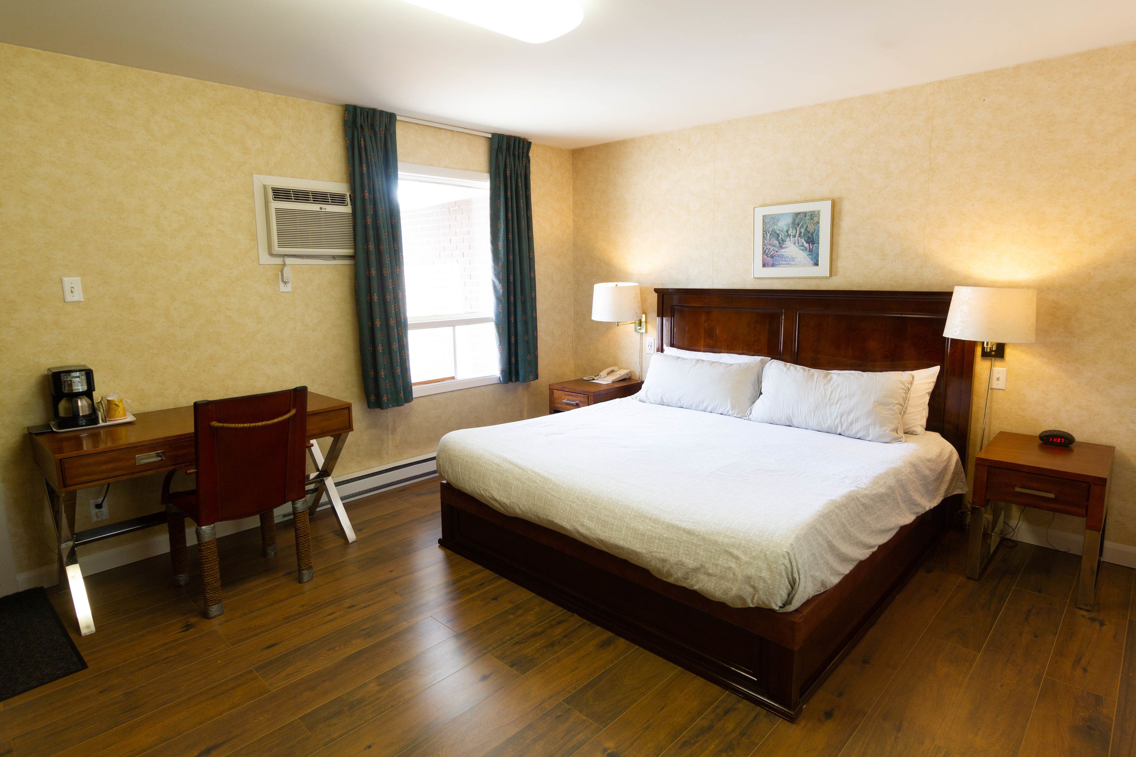 Een hotelkamer met een groot bed, een bureau met stoel, een nachtkastje met lamp en een raam met gordijnen.
