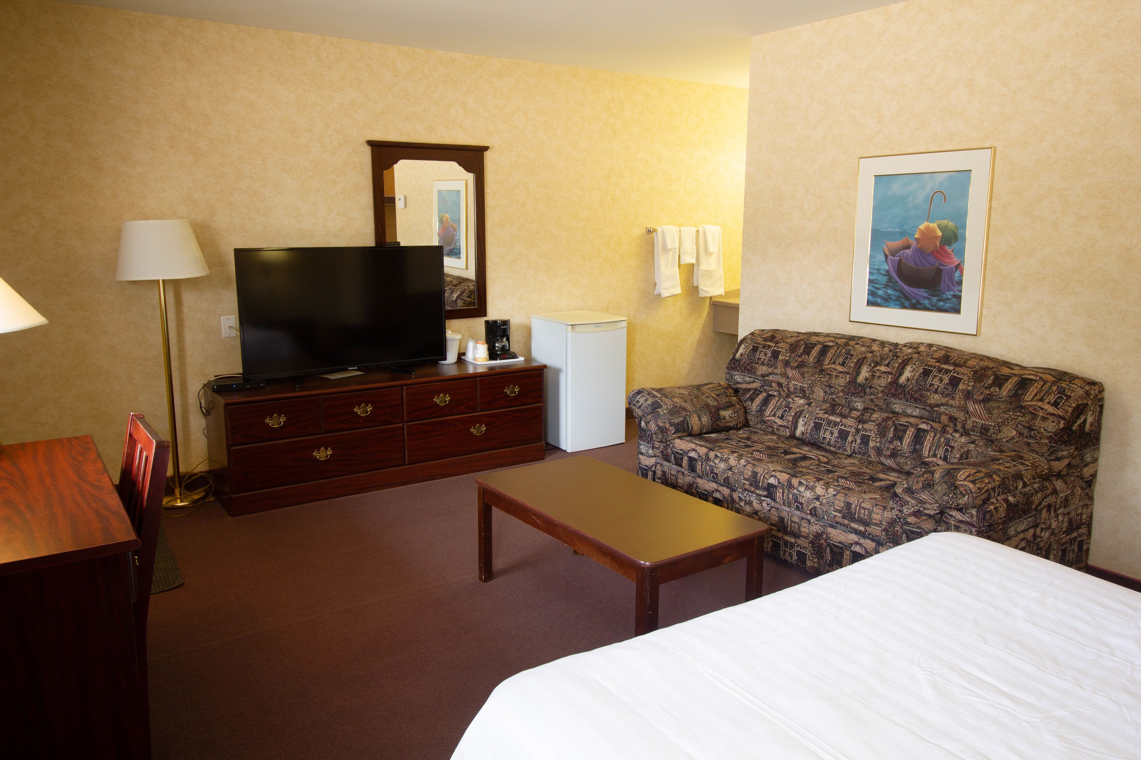A hotel room with a bed, a sofa, a television, a dresser, and a coffee maker.