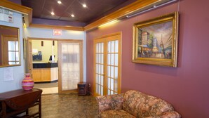 A lobby with a reception desk, a patterned sofa, and a framed painting of a cityscape. - Auberge La Rocaille (Shawinigan)