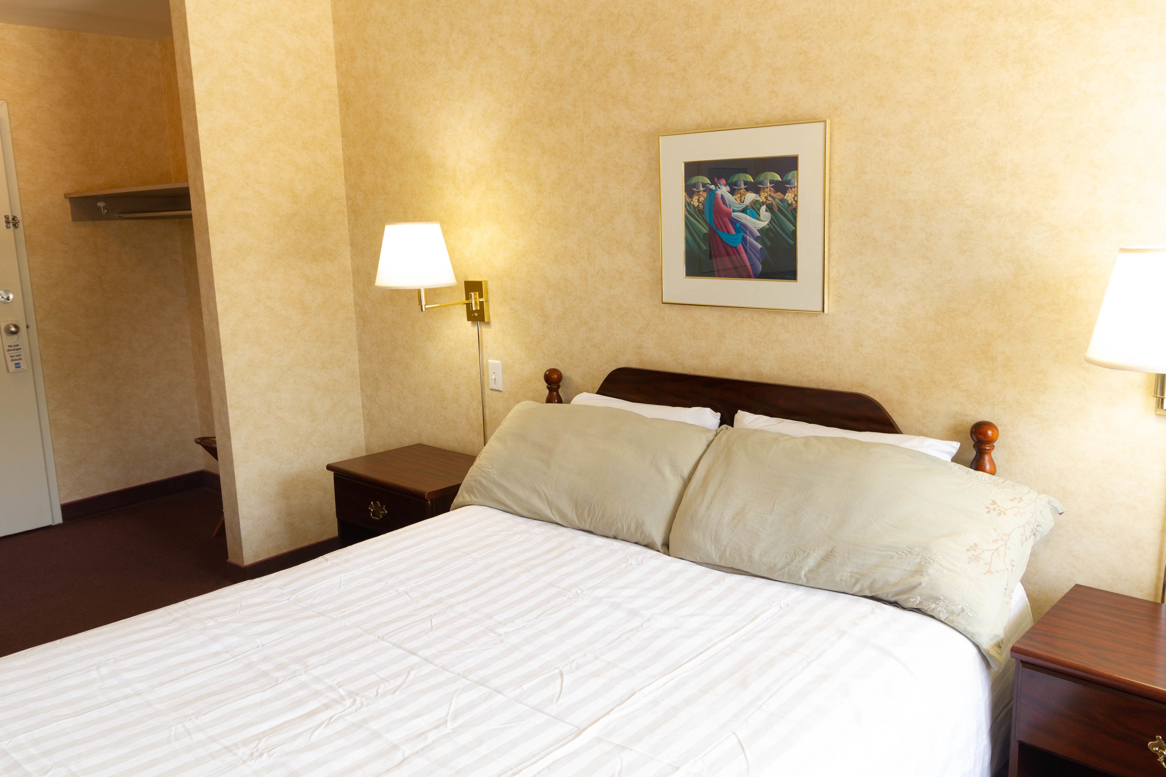 Une chambre d’hôtel avec un grand lit, deux tables de chevet, une petite table, une lampe fixée au mur et un tableau encadré accroché au mur.