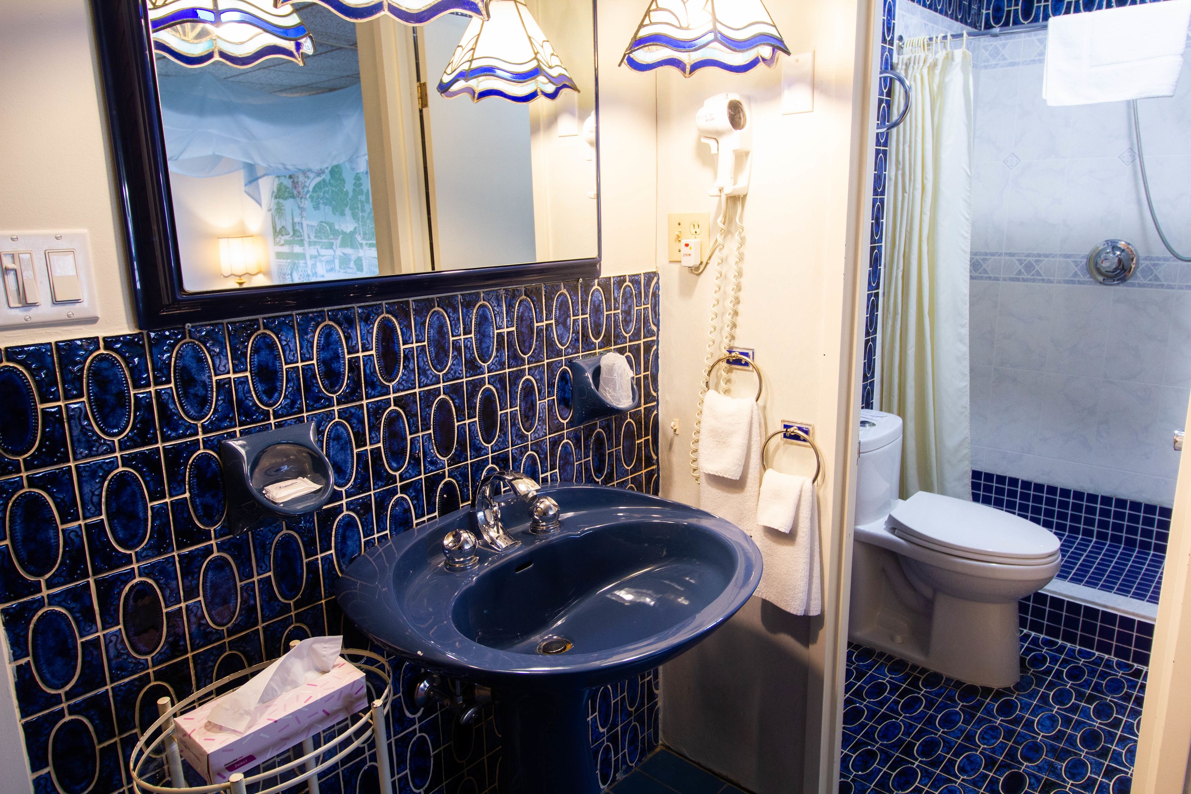 A bathroom with a blue sink, a mirror, a toilet, and a shower.