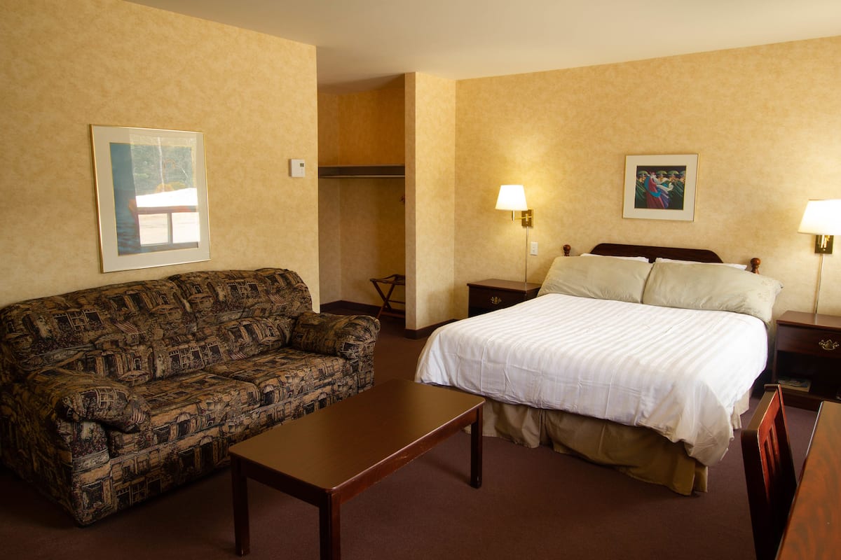 Habitación de hotel con cama, sofá, mesa, dos lámparas y un cuadro en la pared.