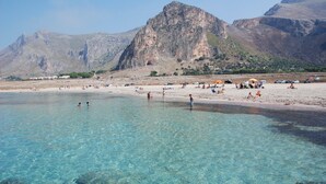 Una spiaggia con acque cristalline turchesi, affioramenti rocciosi e montagne sullo sfondo.