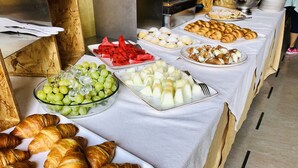 Un tavolo del buffet con diversi cibi, tra cui croissant, anguria, uva e formaggio.