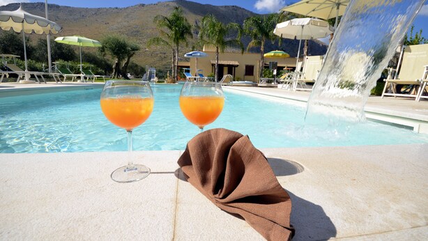 Area piscina con due bicchieri di bevanda arancione, un asciugamano e una fontana.