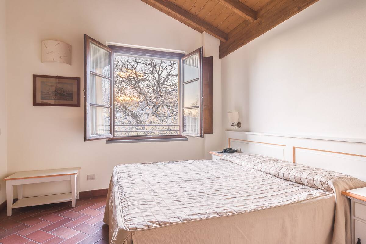 Un dormitorio con una cama grande, una mesita de noche, una ventana con vistas a árboles y un techo de madera.